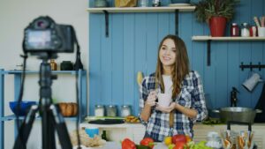キッチンで三脚のカメラに向かって商品を紹介しながらライブ配信する女性